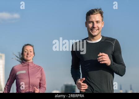 Niedrigen Winkel Oberkörper Blick gegen strahlend blauen Himmel ein Lächeln auf den Lippen schöner Mann Joggen mit seiner Frau in ein Gesundheits- und Fitness-Konzept Stockfoto