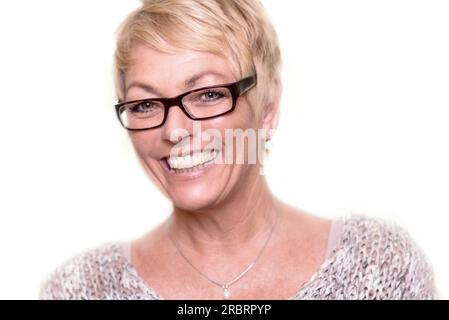 Bild von Kopf und Schultern einer glücklichen, attraktiven blonden Frau mittleren Alters, die eine Brille trägt und mit einem schönen, lebhaften Lächeln in die Kamera schaut Stockfoto