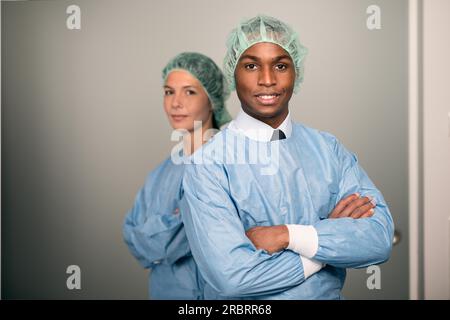 Selbstbewusste männliche und weibliche Mediziner lächeln die Kamera an und tragen blaue Peelings und Sterilitätskappe Stockfoto