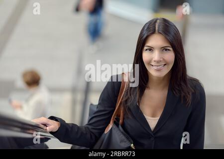 Lächelnde Brünette reitet auf die Rolltreppe im öffentlichen Raum Stockfoto