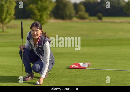 Attraktive Golfspielerin Abholung einen Golfball der Bohrung nach spielte eine gute Note in die Kamera Lächeln Stockfoto