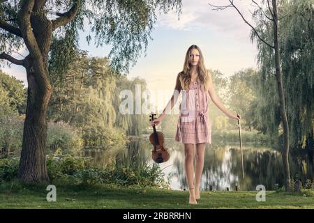 Junge Musikerin mit ihrer Violin, steht am See und schaut in die Kamera Stockfoto