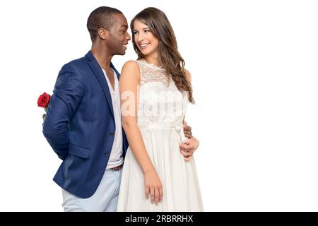 Ein romantischer junger Mann umarmt seine Freundin mit einem liebevollen Lächeln, während er eine überraschende rote Rose hinter seinem Rücken versteckt, Valentinstag, Jahrestag oder Stockfoto