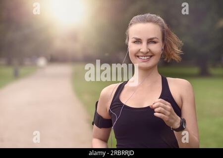 Eine halbe Stelle erschossen eine ziemlich sportliche Frau Joggen im Park mit Kopfhörer und Lächeln in die Kamera, mit Textfreiraum Stockfoto