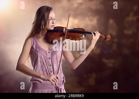 Hübsche junge Violinistin in einem stylischen pinken Outfit, die Geige spielt, während sie ein klassisches Konzert auf der Akademie gibt oder für eine trainiert Stockfoto