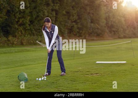 Golfspielerin stehen auf der driving Range am späten Nachmittag am Tag, für den nächsten Schlag konzentrieren Stockfoto