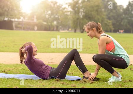 Glücklich athletische Frau lächelte ihre Freundin während tun Curl Up Übung im Park Stockfoto