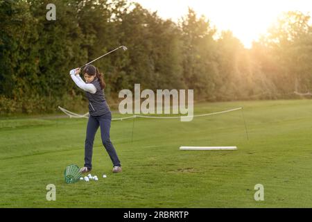Golfspielerin stehend auf der driving Range am späten Nachmittag am Tag, während des Swingens konzentrieren ihr club Stockfoto