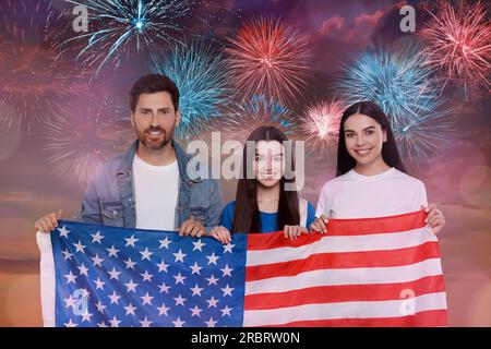 4. Juli - Unabhängigkeitstag Amerikas. Glückliche Familie, die mit Feuerwerk die Nationalflagge der Vereinigten Staaten gegen den Himmel hält Stockfoto