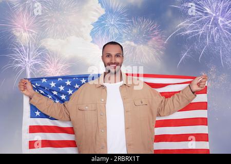 4. Juli - Unabhängigkeitstag Amerikas. Glücklicher Mann, der die Nationalflagge der Vereinigten Staaten gegen den Himmel hält, mit Feuerwerk Stockfoto