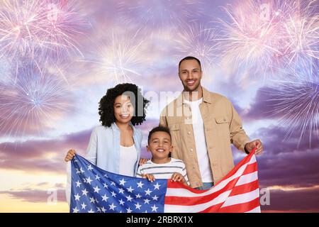 4. Juli - Unabhängigkeitstag Amerikas. Glückliche Familie, die mit Feuerwerk die Nationalflagge der Vereinigten Staaten gegen den Himmel hält Stockfoto