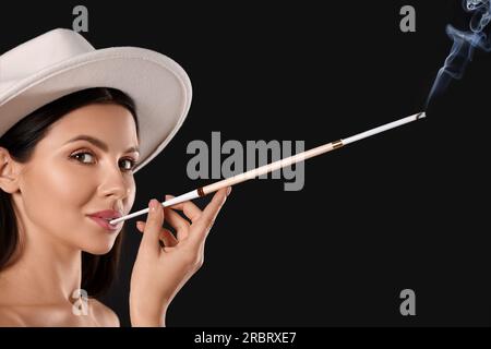 Frau mit langem Zigarettenhalter zum Rauchen auf schwarzem Hintergrund Stockfoto