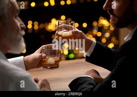 Männer mit Whiskey-Gläsern, die sich an einem Holztisch in der Bar unterhalten Stockfoto