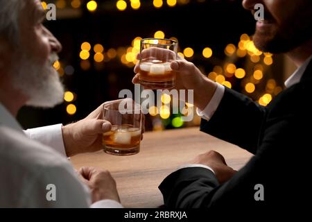 Männer mit Whiskey-Gläsern, die sich an einem Holztisch in der Bar unterhalten Stockfoto