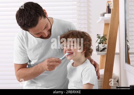 Vater hilft seinem Sohn, im Bad Zähne zu putzen Stockfoto