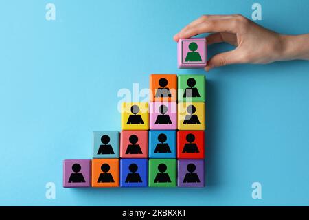 Frau, die Würfel mit grünem Menschensymbol auf andere stellt, mit schwarzen auf hellblauem Hintergrund, Nahaufnahme Stockfoto