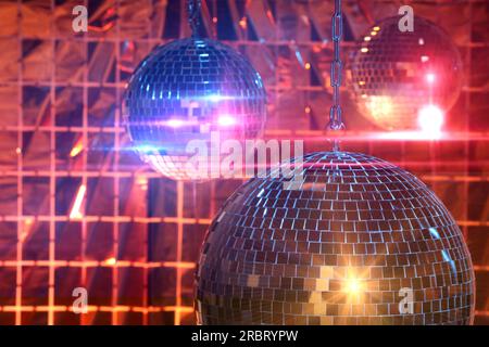 Glänzende Disco-Bälle gegen einen Partyvorhang unter farbigen Lichtern Stockfoto