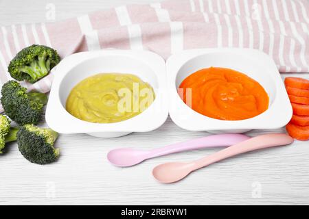 Behälter mit gesunder Babynahrung, Löffel und Zutaten auf weißem Holztisch Stockfoto