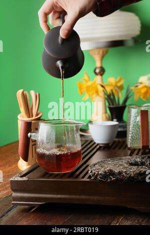 Frau, die frisch gebrühten pu-erh-Tee in den Krug am Holztisch gießt, Nahaufnahme Stockfoto