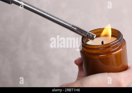 Frau, die Kerze mit Gasanzünder an graue Wand zündet, Nahaufnahme Stockfoto