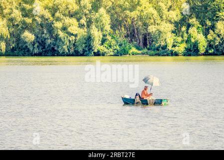 Kiew, Ukraine, 25. August 2015, Ein Mann, Ein Fischer, auf einem Boot auf dem Dnjepr-Fluss von Kiew. Er benutzt einen Schirm, um sich vor der Wärme zu schützen Stockfoto