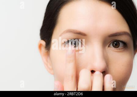 Eine Frau, die gerade eine Einweg-Kontaktlinse aus Plastik in ihr Auge steckt, um ihr Sehvermögen zu korrigieren, hat sie am Ende ihres Fingers vor ihrem Gesicht ausgeglichen Stockfoto