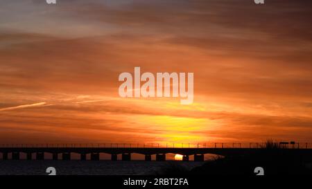 Orangefarbener, dramatischer Sonnenaufgang über der Great Belt Bridge, die die Ostsee überquert, im Frühling Stockfoto