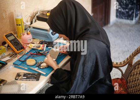 Eine palästinensische Frau Walaa Hammad repariert Smartphones in der Empfangshalle ihrer Familie im Al-Shati-Flüchtlingslager in West Gaza City. Die palästinensische Walaa Hammad, 26, startete ihr Projekt zur Reparatur von Smartphones für Frauen nur in dem bescheidenen und einfachen Haus ihrer Familie im Zentrum des Flüchtlingslagers Al-Shati westlich von Gaza. Hammad bietet einen Telefonreparaturservice für Frauen an, die Angst davor haben, männlichen Technikern ihre Fotos und Konten auf Social-Media-Plattformen zeigen zu lassen. Und mit den schlechten und schwierigen wirtschaftlichen Bedingungen, die die Bewohner des Gazastreifens erleiden, der Zunahme der Arbeitslosigkeit und der l Stockfoto