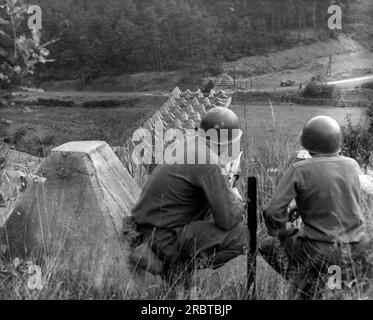 Deutschland, 1944, zwei amerikanische Soldaten, die auf eine lange Reihe von "Drachenzähnen" Betongeräten herabsehen, um die Invasoren der Panzer an den Siegfried-Linien zu stoppen. Stockfoto