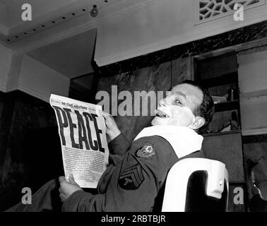 Paris, Frankreich: 14. August 1945 Ein Sergeant in Paris unterbricht seine Rasur in einem Friseursalon und hält die neueste Ausgabe von "The Stars and Stripes", die die Kapitulation Japans mit der Schlagzeile "FRIEDEN" verkündet. Stockfoto