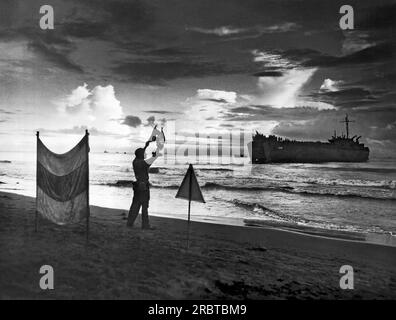 Sarmi, Niederländisch-Neuguinea, 17. Mai 1944 Ein Coxswain der Küstenwache leitet bemannte und truppengepackte LSTs mit Semaphorsignalen an ihre Strandpositionen. Stockfoto