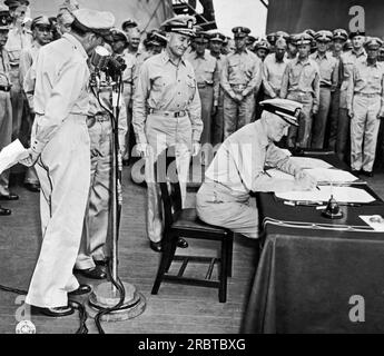 Tokio, Japan: 1. September 1945 Flottenadmiral Chester Nimitz signiert während der japanischen Kapitulationszeremonie an Bord der USS Missouri in der Bucht von Tokio für die Vereinigten Staaten. General der Armee Douglas MacArthur steht links am Mikrofon. Stockfoto