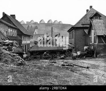 Sankt Andreasberg, Deutschland, 14. April 1945 Ein US-Panzer schwingt auf der anderen Straßenseite und bietet Infanterie-Soldaten der 1. Infanteriedivision, USA, Deckung Erste Armee, die Scharfschützen in Gebäuden sucht. Stockfoto