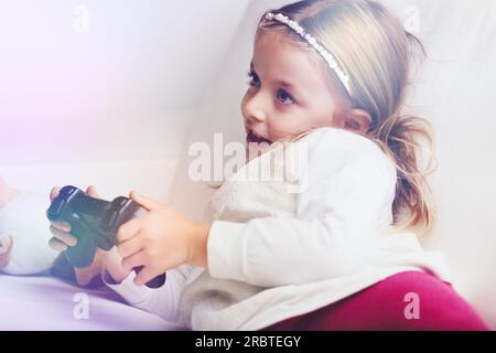 Ein junges Mädchen spielt fröhlich Videospiele, mit elterlicher Begleitung, die eine sichere Online-Erkundung ermöglicht Stockfoto