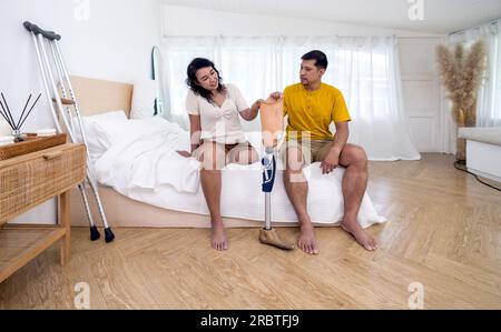 Eine asiatische Frau mit Prothesen, bionischem Bein, prothetischen Gliedmaßen, die zusammen mit ihrem Mann im Schlafzimmer zu Hause sitzen. Stockfoto