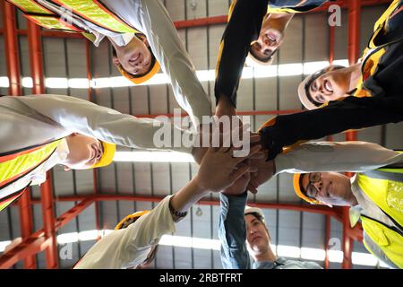 Gruppe von männlichen und weiblichen Fabrikarbeitern, die sich nach dem Abschlussgespräch zusammentun. Alle tragen Schutzkleidung und Helm. Arbeiter, die im Gerichtsmediziner arbeiten Stockfoto