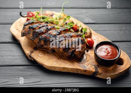 Heiße gegrillte Spare Ribs vom Sommer BBQ serviert mit frischen Tomaten auf Holzbrett Stockfoto