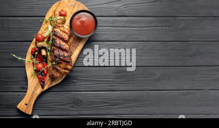 Gegrillte Schweinerippchen mit Kirschtomaten, Pfeffer und Barbecue-Sauce auf Holzbrettern vor dunklem Hintergrund. Draufsicht Stockfoto