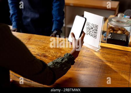 Die Hand einer afroamerikanischen Frau scannt den qr-Code mit dem Smartphone im Café Stockfoto