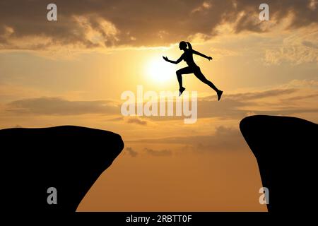 Konzept des Erreichens von Lebens- und Geschäftszielen. Silhouette einer Frau, die bei Sonnenaufgang über den Abgrund springt Stockfoto