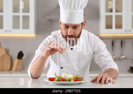 Professioneller Koch salzt köstlichen Salat am Marmortisch in der Küche Stockfoto