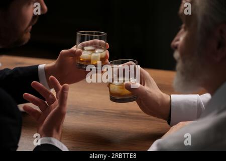 Männer mit Whiskey-Gläsern, die sich an einem Holztisch in der Bar unterhalten Stockfoto