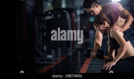 Fitnesstrainer hilft Frau beim Üben von Kurzhanteln. Personal Trainer im Fitnessraum Stockfoto