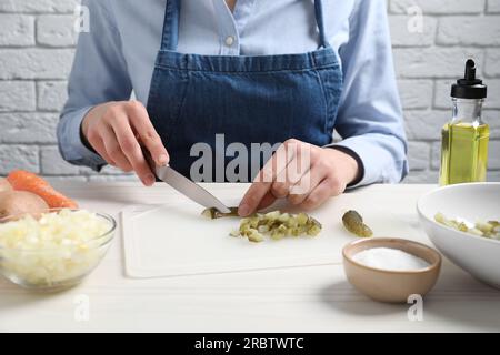 Eine Frau schneidet eingelegte Gurken auf einem weißen Holztisch, Nahaufnahme. Ich koche Vinaigrette-Salat Stockfoto