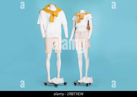 Damen- und Männerpuppen mit Turnschuhen in weißen T-Shirts, stilvollen Shorts und orangefarbenen Pullover auf hellblauem Hintergrund Stockfoto
