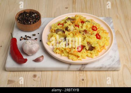 Köstlicher Pilaf mit Fleisch und Zutaten auf einem Holztisch Stockfoto