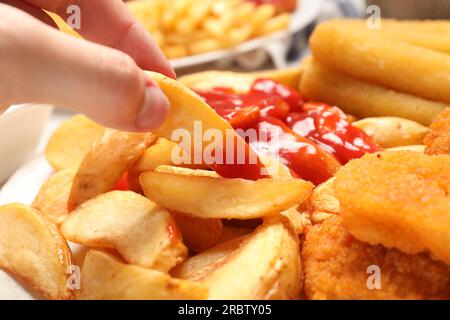 Eine Frau, die leckeren gebackenen Kartoffelkeil mit Ketchup am Tisch nimmt, Nahaufnahme Stockfoto