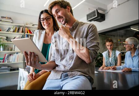 Lächelnd treffen sich verschiedene Kollegen in einem Brainstorming in der Vorstandsetage, um gemeinsam Finanzstatistiken zu diskutieren Stockfoto