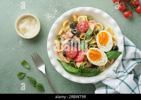 Italienischer Nudelsalat. Orekchiette-Pasta mit Thunfisch, Tomatenkirsche, Oliven, Basilikum und Parmesan auf grünem Stein- oder Betonboden. Trad Stockfoto