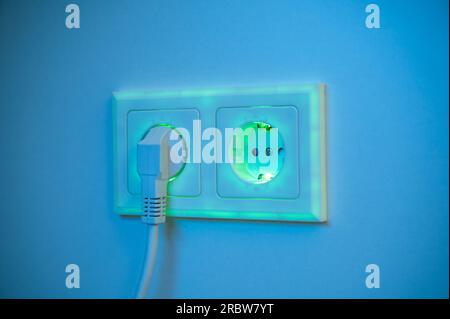 Grün beleuchtete Buchse mit eingestecktem Stecker zur Darstellung des Stromverbrauchs und der elektrischen Energie aus einer Steckdose, die umweltfreundliche und saubere Energie liefert Stockfoto